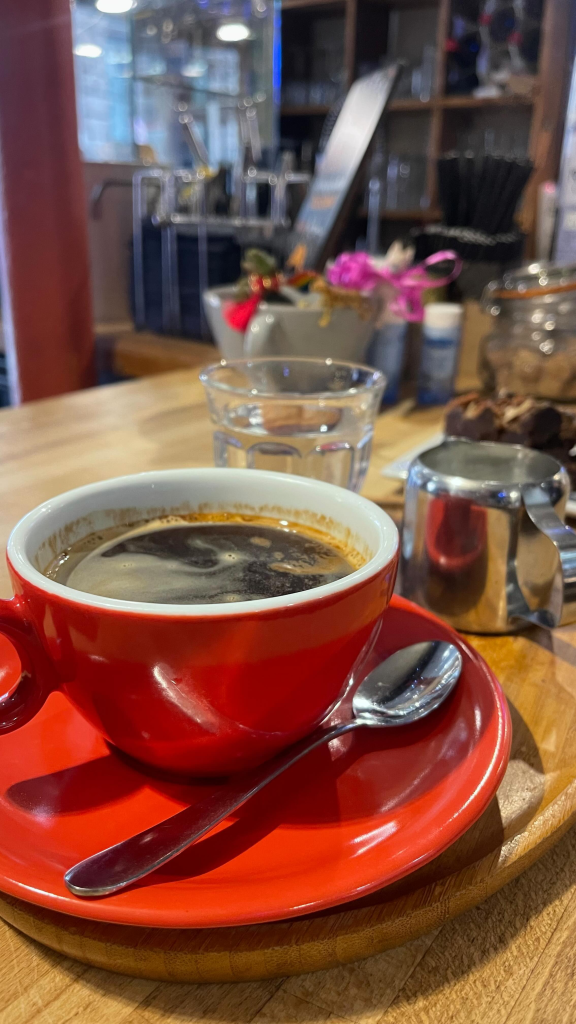 Red cup of coffee on wooden table in a cosy café setting, with silver spoon and milk jug nearby