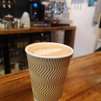 Paper cup with latte art on a wooden counter in a cosy café setting