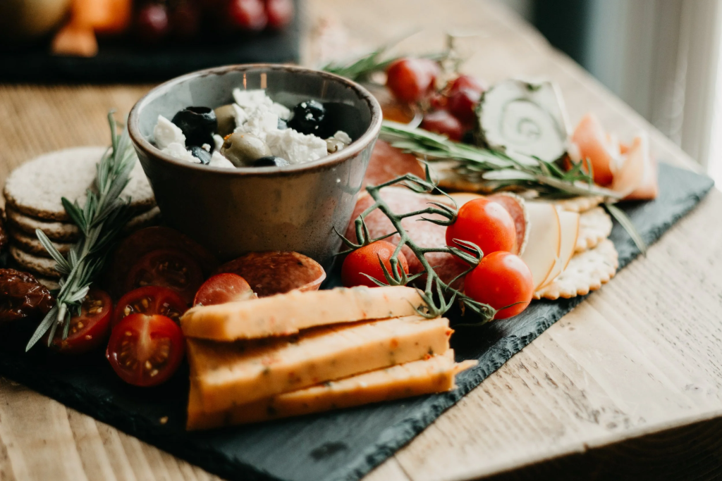 Cheese and charcuterie platter with olives, tomatoes, and crackers on rustic wooden table setting