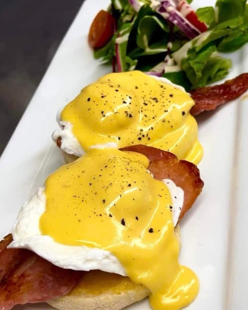 Eggs Benedict with crispy bacon and creamy hollandaise sauce, garnished with salad, served on a white plate