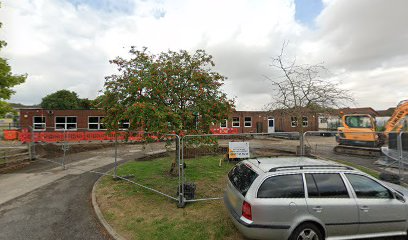 Construction site with a fenced-off building, tree, parked car, and excavator under a cloudy sky