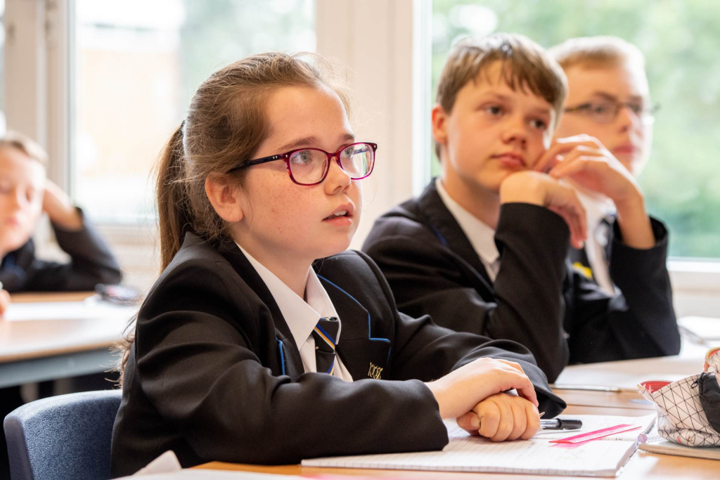 Students in a classroom wearing school uniforms, attentively listening and taking notes during a lesson