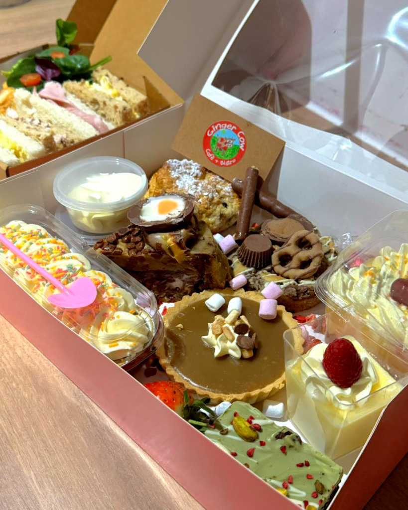 Assorted afternoon tea treats in a box with sandwiches, cakes, desserts, and scones from a café in the UK