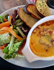Baked cheese dish with salad and toasted bread slices on a white plate, featuring fresh greens and vegetables