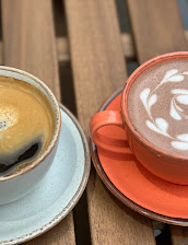 Two cups of coffee on a wooden table, one with latte art in an orange cup, the other black in a white cup