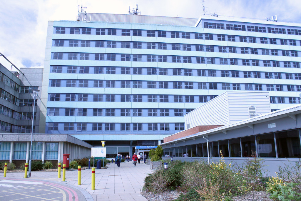 Large hospital building exterior with multiple windows and people walking on pavement in front