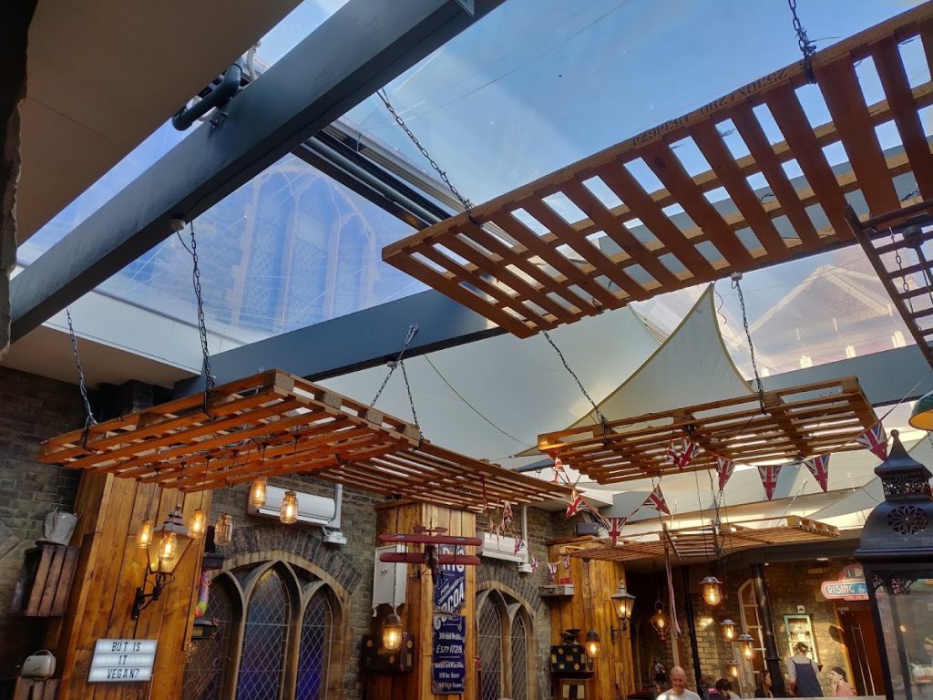 Rustic café interior with wooden crates, vintage lighting, and bunting under a glass roof in a cosy atmosphere