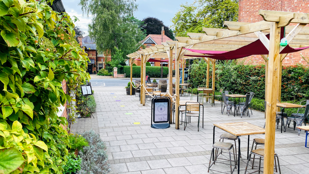 Outdoor café seating with wooden pergolas and greenery in a charming village setting